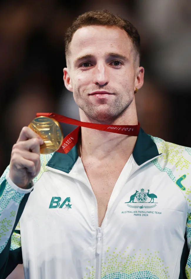 Australian Paralympic athlete in a team jacket holding a Paris 2024 gold medal and smiling.