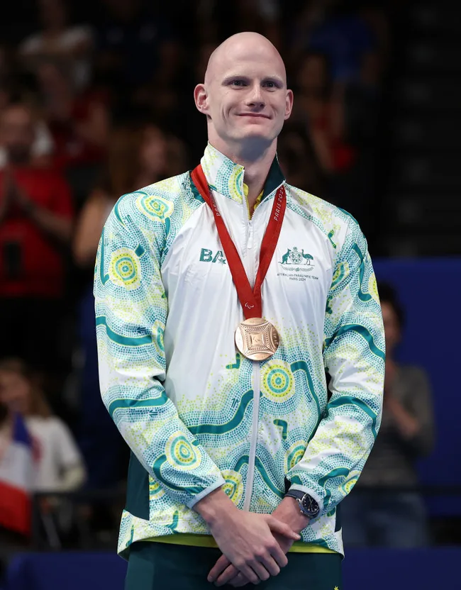 Australian Paralympic athlete proudly wearing a medal and team jacket at an award ceremony.
