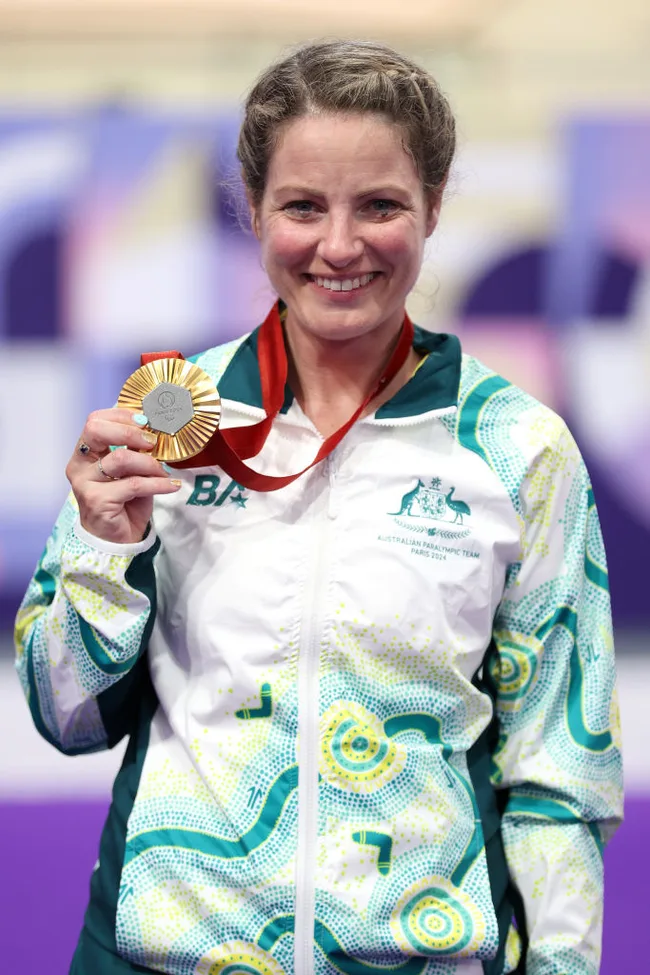 Athlete in an Australian jacket holding a gold medal and smiling at a sports event.