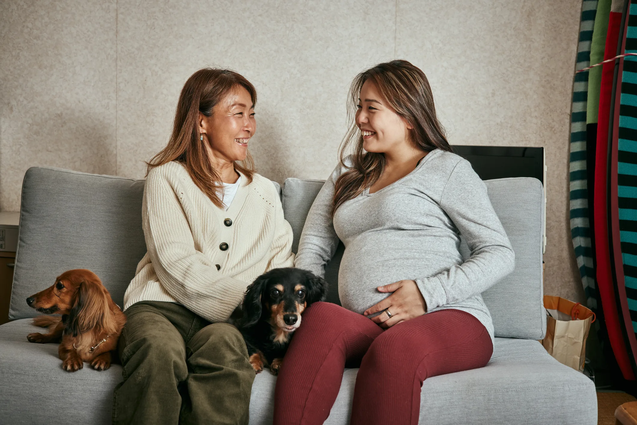 mother and her pregnant daughter sitting together on the sofa with two dachsund dogs