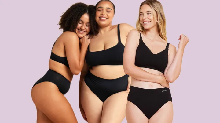 Three women in black bras and underwear smiling on a light purple background.