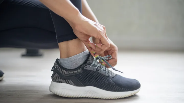 Person tying shoelaces of a black sneaker with a white sole, wearing grey socks and black leggings.