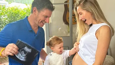 Family celebrates pregnancy; father holds ultrasound, child points to mother's belly, all smiling.