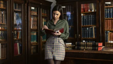 Woman reading a book in a cozy library, surrounded by wooden bookshelves filled with colorful books.