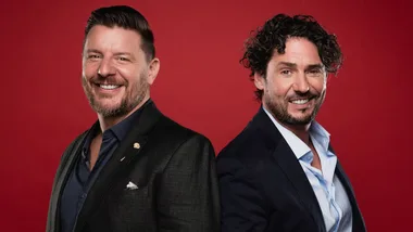 Two smiling men in suits standing back-to-back against a red background.