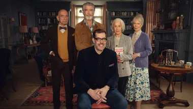 Five people pose indoors; one holds a book by Richard Osman. Vintage decor in the background.