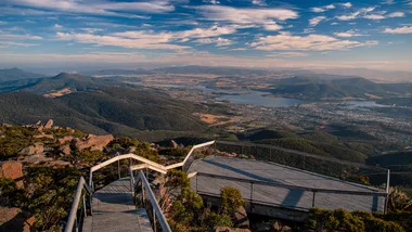 Scenic view from Mount Wellington, Tasmania, overlooking Hobart city, with blue skies and distant mountains.