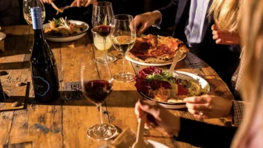 Dining table with pizza, salad, and wine; people enjoying a meal together.
