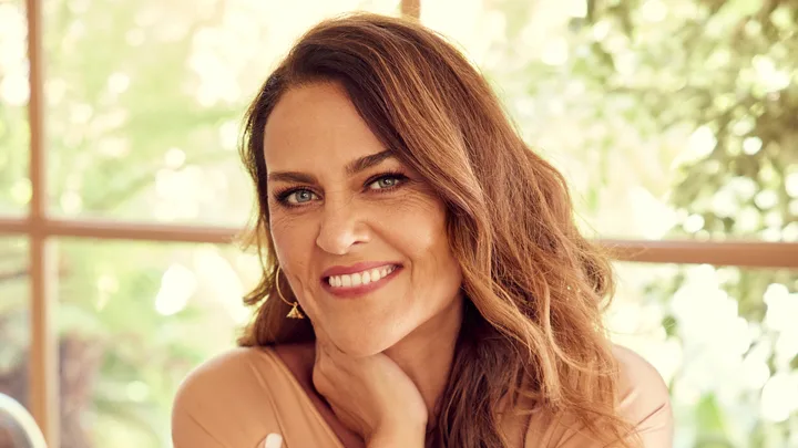 Smiling woman with long brown hair against a blurred green background.