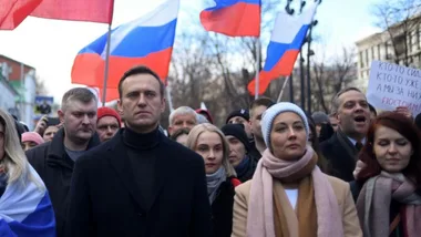 Protesters holding Russian flags march in a large crowd on a city street.