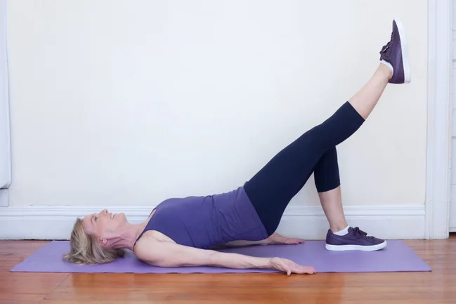 Woman performing a single-leg bridge exercise on a yoga mat indoors.
