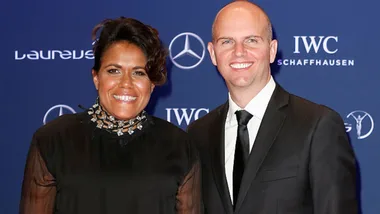 Two people smiling at a Laureus event, standing in front of a backdrop with logos.