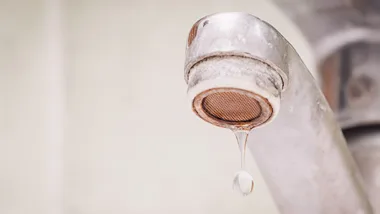 Close-up of a faucet with a single water droplet hanging from the spout.