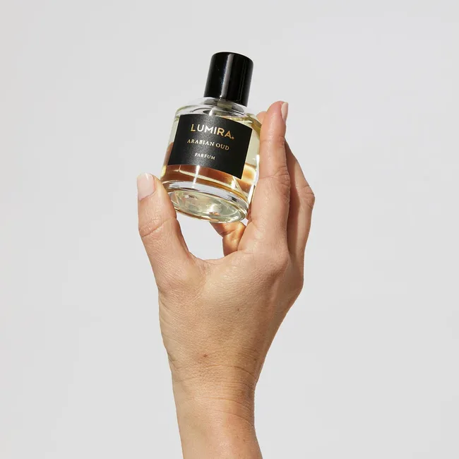 Hand holding a Lumira Arabian Oud perfume bottle against a neutral background.
