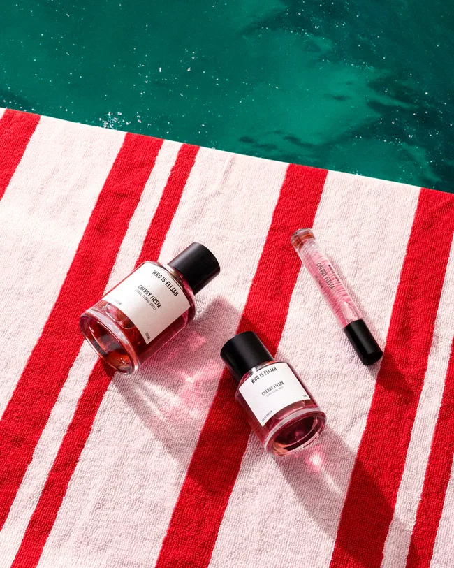 Perfume bottles labeled "Who is Elijah" on a red and white striped towel beside a pool.