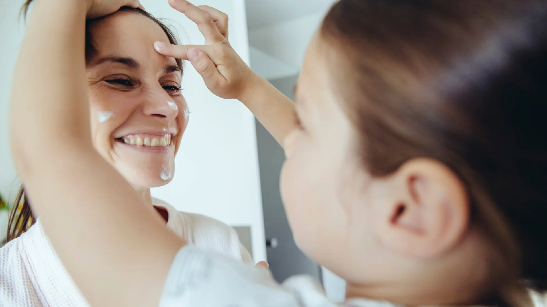 Child putting face cream on woman