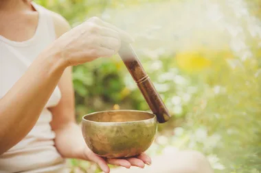 Person holding and using a Tibetan singing bowl outdoors.