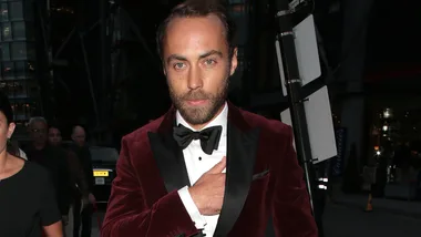 Man in a burgundy tuxedo on a city street at night, looking at the camera.