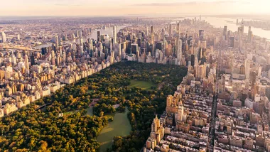 Aerial view of Central Park surrounded by New York City skyscrapers at sunset.