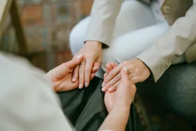 Two people sitting close, gently holding hands in a comforting manner, suggesting support or empathy.