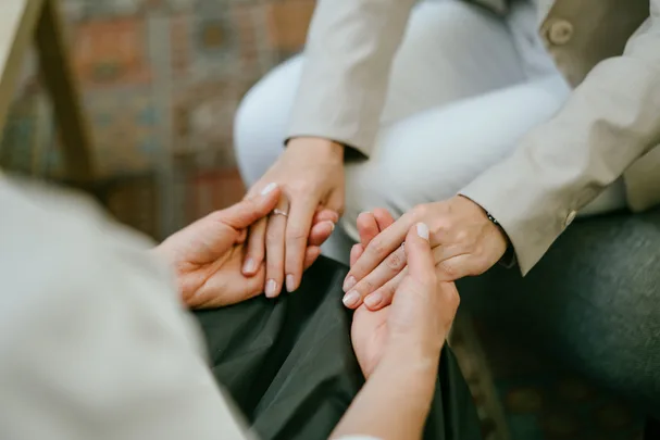 Two people sitting close, gently holding hands in a comforting manner, suggesting support or empathy.