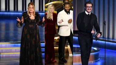 Three presenters on stage at an award show, one in a black dress, another in red with a white tux, and a man in black.