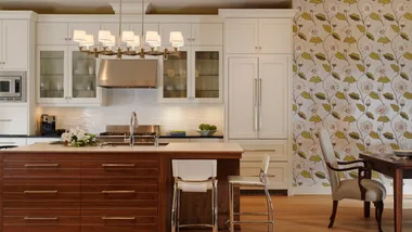 Modern kitchen with white cabinets, stainless steel appliances, floral wallpaper, and a wooden dining table with chairs.