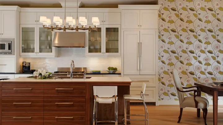 Modern kitchen with white cabinets, stainless steel appliances, floral wallpaper, and a wooden dining table with chairs.
