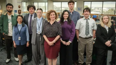 Cast of the TV show "Utopia," featuring nine people standing in an office setting.