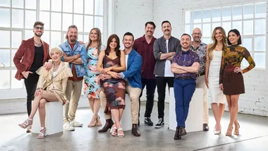 Group photo of 12 men and women in colorful outfits standing and sitting in a bright room.