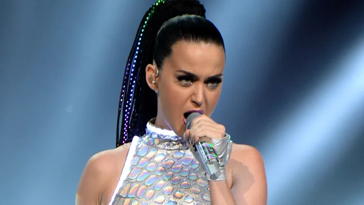 A performer in a shimmering outfit passionately singing on stage with a microphone.