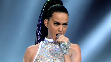 A performer in a shimmering outfit passionately singing on stage with a microphone.