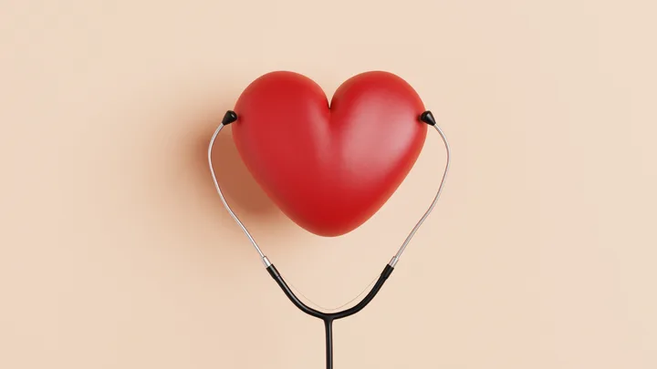 Red heart attached to a stethoscope on a peach background, symbolizing heart health and medical care.