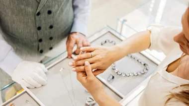 Person trying on a ring at a jewelry store, assisted by a gloved attendant.