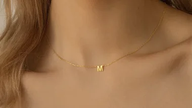 A gold necklace with an "M" pendant worn on a woman's neck.