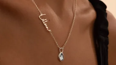 Silver necklace with "Lillian" nameplate and teardrop pendant on a person's neck.