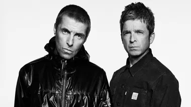 Two men in black and white portrait; one in a shiny jacket, the other in a collared shirt. Both have serious expressions.