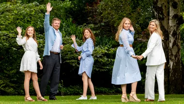 A family in stylish clothing waves while standing in a lush green garden.