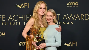Two women smiling, one holding a star-studded award at AFI event, black backdrop with AMC and AFI logos.