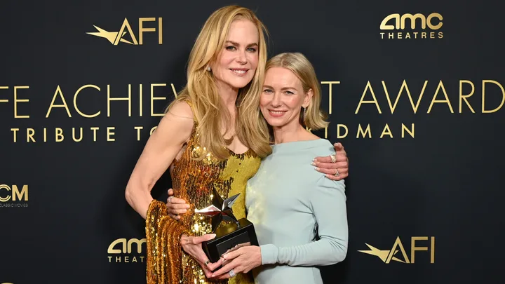 Two women smiling, one holding a star-studded award at AFI event, black backdrop with AMC and AFI logos.