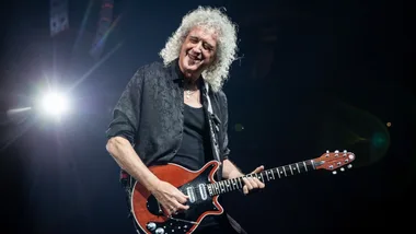 Guitarist with curly hair playing an electric guitar on stage, bright light in the background.