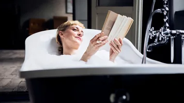 Woman relaxing in a bubble bath while reading a book, enjoying a moment of tranquility.