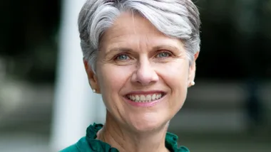 Smiling woman with short gray hair and green top, outdoors.