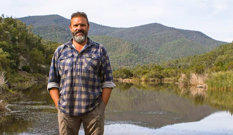 Richard Swain stands in front of an Australian landscape.