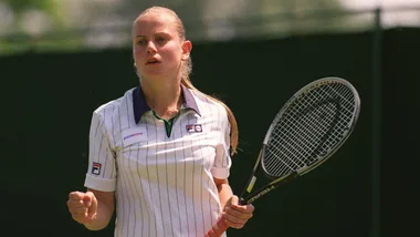 A tennis player in action, wearing a white Fila shirt, holding a racket, with a focused expression.
