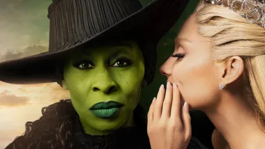 Two women in dramatic makeup and costumes, one with green skin and black hat, the other whispering, wearing a crown.