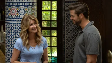 Two people smiling and talking indoors, standing near a patterned blue and white tiled column.