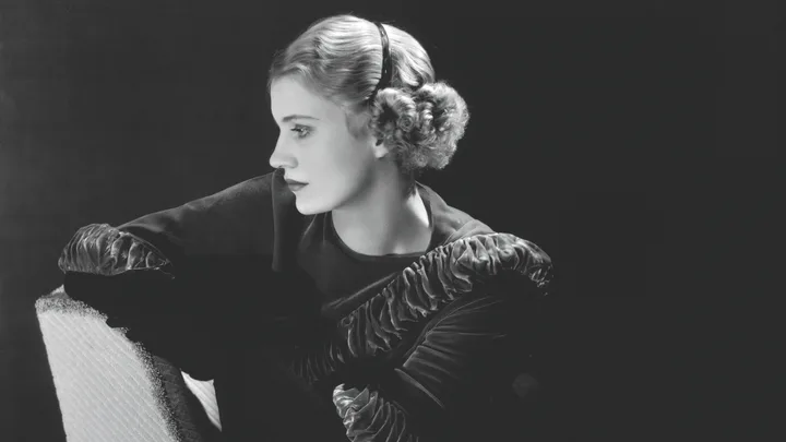 Black and white portrait of a woman in profile with headband and wavy hair, looking thoughtfully into the distance.
