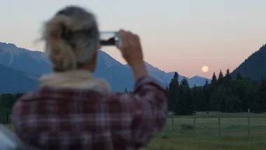 A person taking a photo of a moonrise over a mountain landscape with a smartphone.