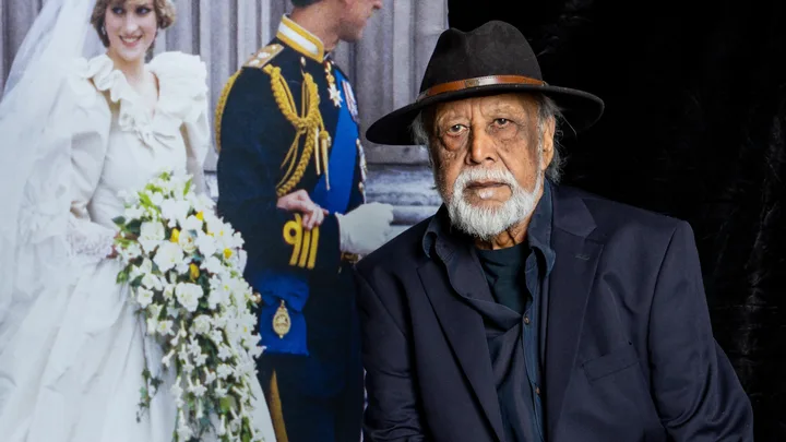 Man in a hat and suit in front of a photograph of a bride and groom, possibly a royal wedding scene.